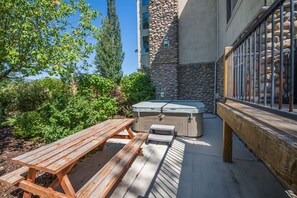 An outdoor patio with a hot tub, wooden picnic table, and stone wall. - Comfy Large Townhome with private hot tub (Eden)