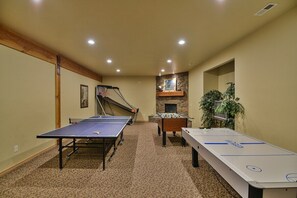 A room with a ping pong table, foosball table, and a fireplace.