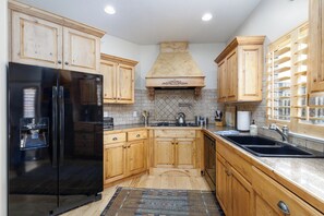 Una cocina con armarios de madera, un refrigerador negro, salpicadero de azulejos y una ventana con repisa.