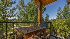 A wooden deck with a table and chairs, surrounded by a metal railing, overlooking a lush green landscape.