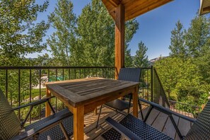 A wooden deck with a table and chairs, surrounded by a metal railing, overlooking a lush green landscape. - Comfy Large Townhome with private hot tub (Eden)