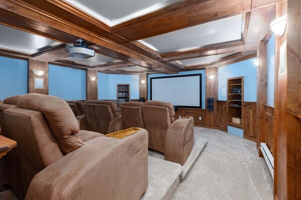 Una sala de cine en casa con paneles de madera, una pantalla grande y varias zonas de estar.