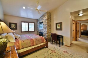 A bedroom with a bed, a desk, a chair, a stone wall, and a ceiling fan. - Comfy Large Townhome with private hot tub (Eden)