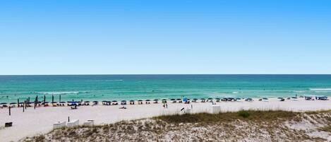 A beach with white sand, clear blue water, and a few umbrellas.