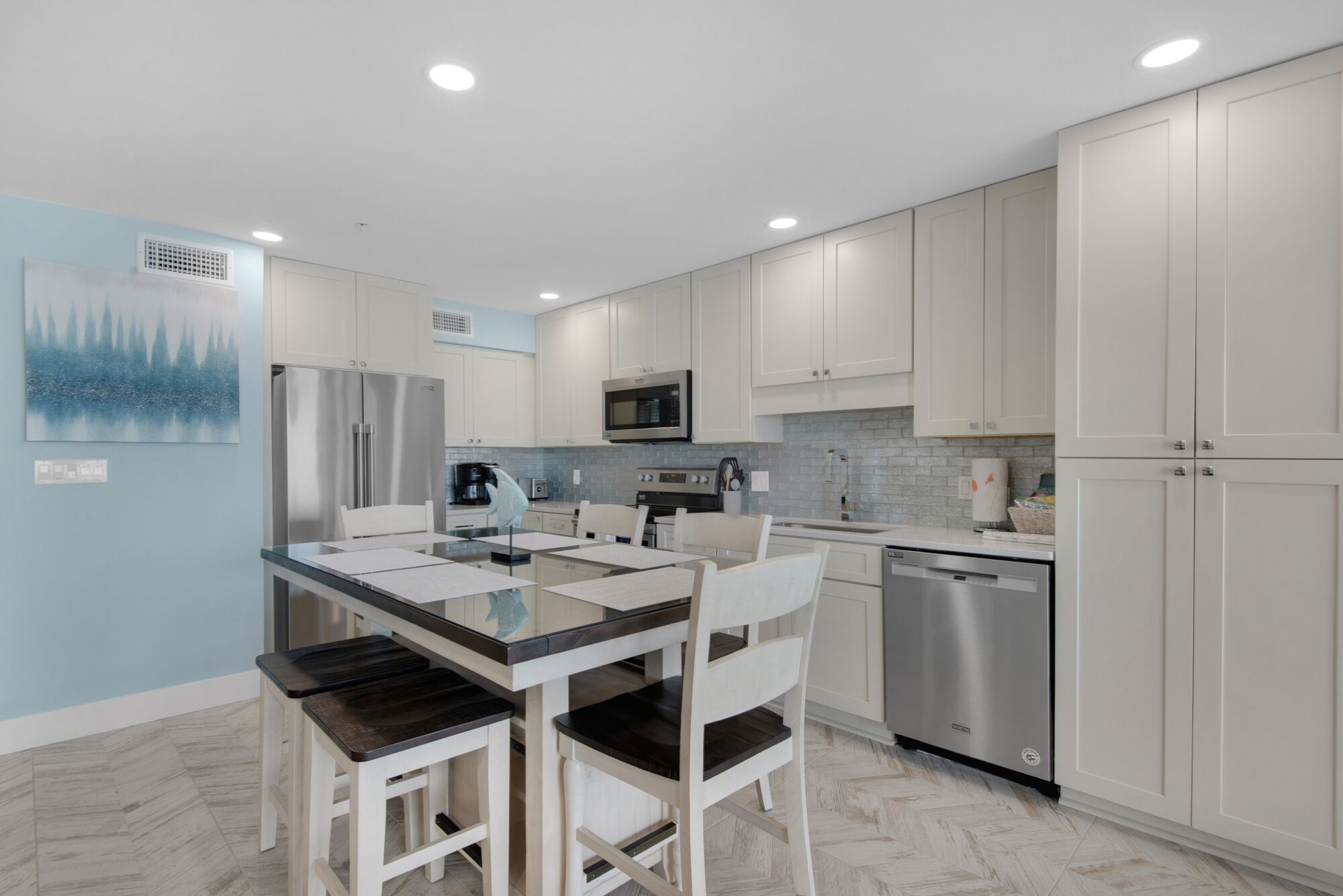 Una cocina moderna con armarios blancos, electrodomésticos de acero inoxidable y una mesa de comedor de vidrio.