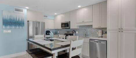 Una cocina moderna con armarios blancos, electrodomésticos de acero inoxidable y una mesa de comedor de vidrio.