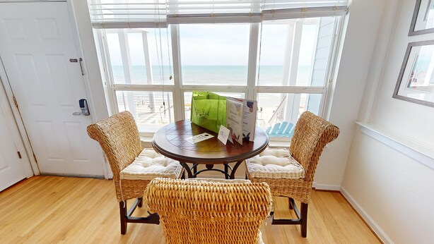 Een kamer met uitzicht op zee, met rieten stoelen, een ronde tafel en een groene tas op de tafel.