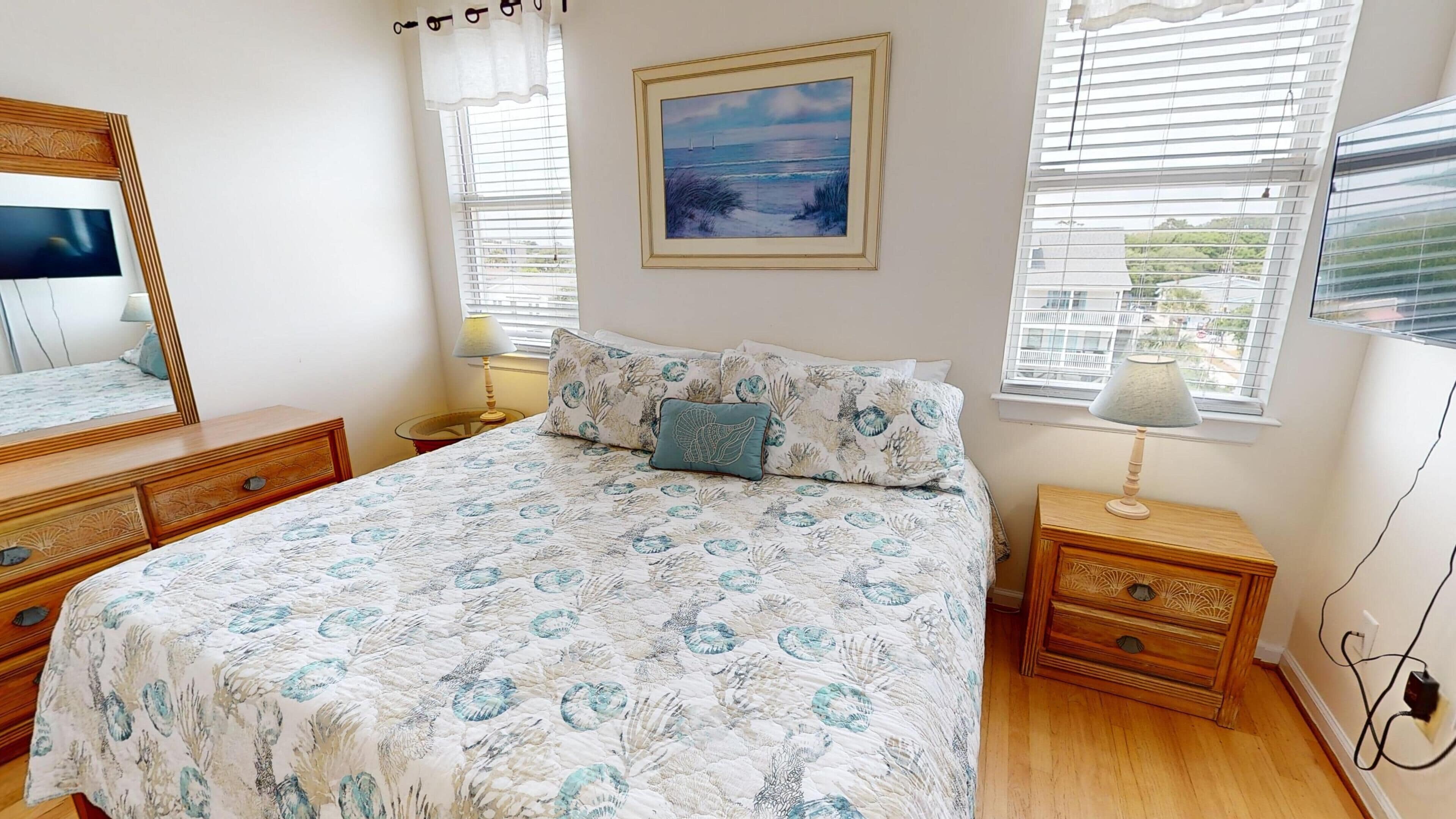 A bedroom with a bed, a bedside table, a lamp, a dresser, a mirror, and a painting on the wall.