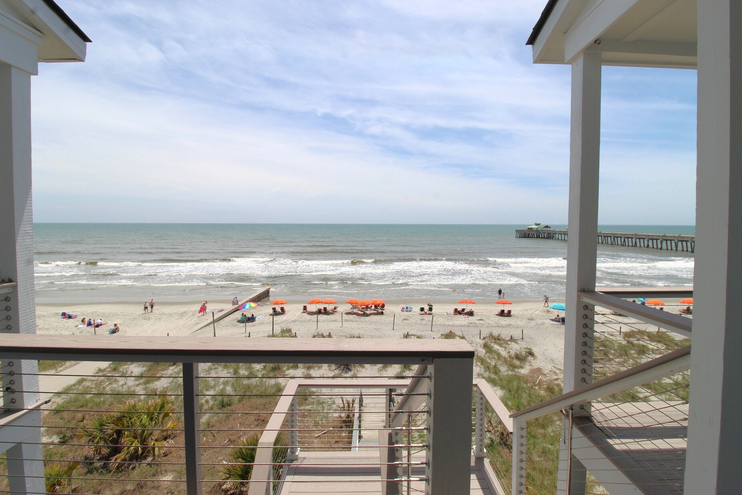 A beach view from a balcony with a pier in the distance.