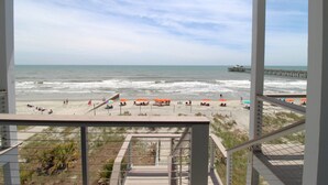 Uitzicht op het strand vanaf een balkon, met een pier in de verte.