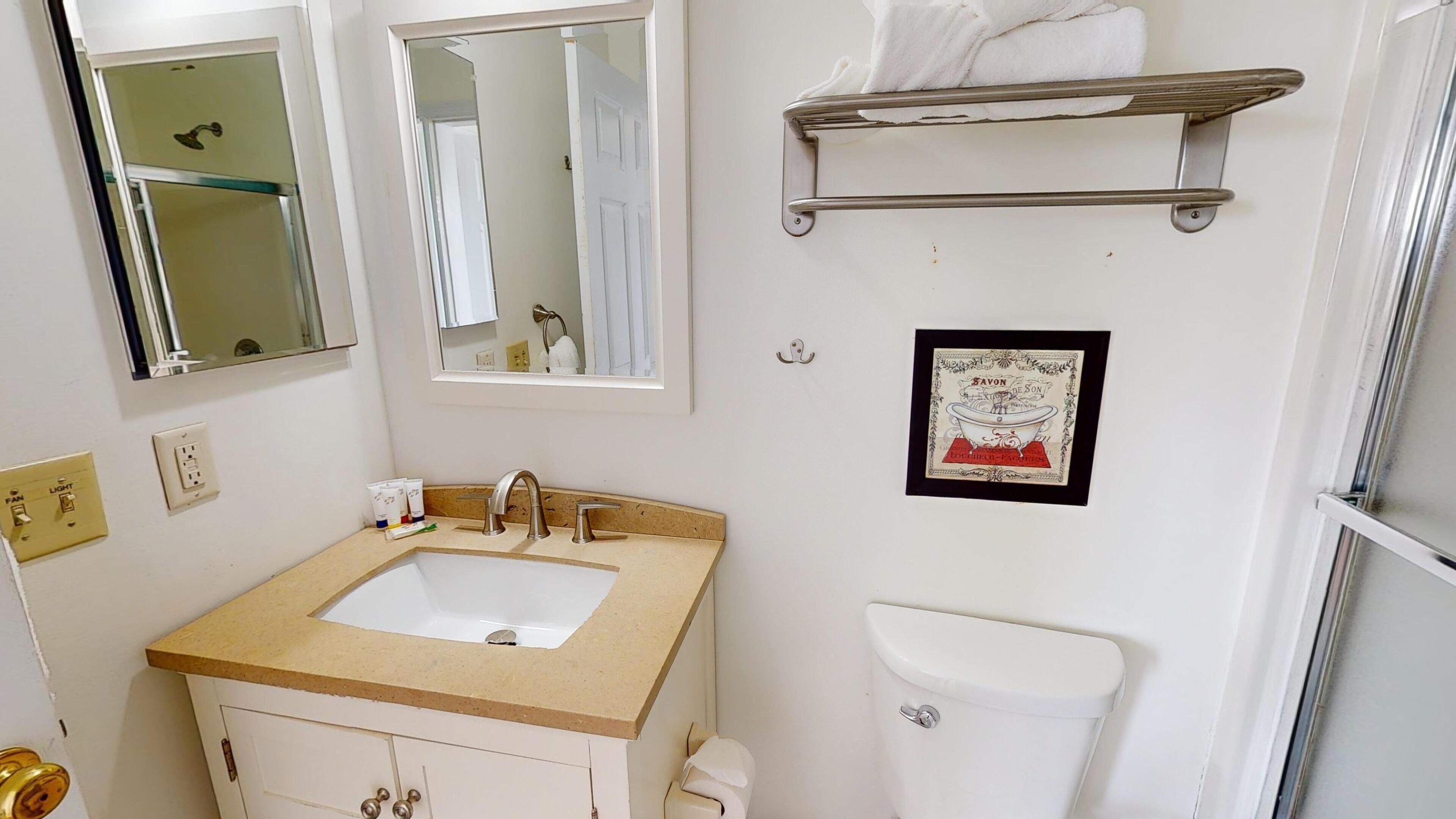 Un baño con lavamanos, dos espejos, inodoro y toallero.