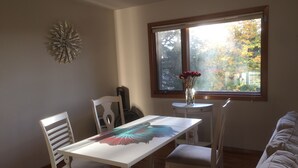 A dining area with a white table, chairs, a decorative wall piece, a window with a view of trees, and a vase with flowers on a small table. - Bellevue Retreat - Bellevue,  East of Seattle, WA (Bellevue)