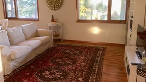A living room with a white sofa, a patterned rug, a small side table with a fruit bowl, and a decorative wall piece. - Bellevue Retreat - Bellevue,  East of Seattle, WA (Bellevue)