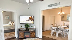 A living room with a TV, a fireplace, a dining area with a chandelier, and a hallway leading to a bedroom. - Historic Corner Cottage - charming 3 bedroom walking distance to waterfront (Beaufort)
