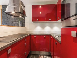 Una cocina moderna con gabinetes rojos, una campana extractora de acero inoxidable y un horno empotrado.