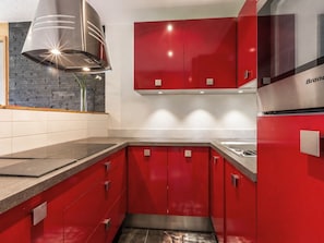 Une cuisine moderne avec des meubles de couleur rouge, une hotte de cuisine en acier inoxydable et un four encastré.
