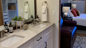 A modern bathroom with a large mirror, two sinks, and a vanity with drawers. There is a potted plant on the vanity and toiletries on the counter. - Inviting Ski In/Ski Out Condo. Covered Parking. Renovated! Heated Pool/Hot Tubs! (Park City)