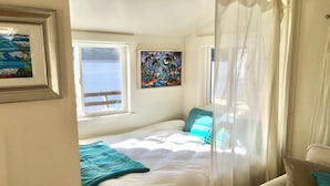 A bedroom with a bed, a window, a painting, and a chair. - Secluded Overwater Eco-Cottage on Private Beach (Vashon)