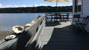 A wooden deck with a railing, a table with chairs, and an umbrella. - Secluded Overwater Eco-Cottage on Private Beach (Vashon)