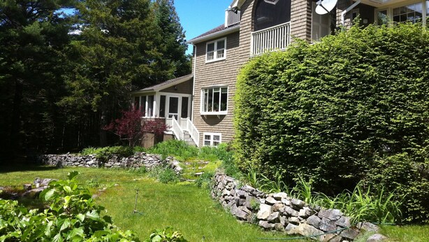 Une maison à deux étages avec un mur en pierre et un jardin bien entretenu.