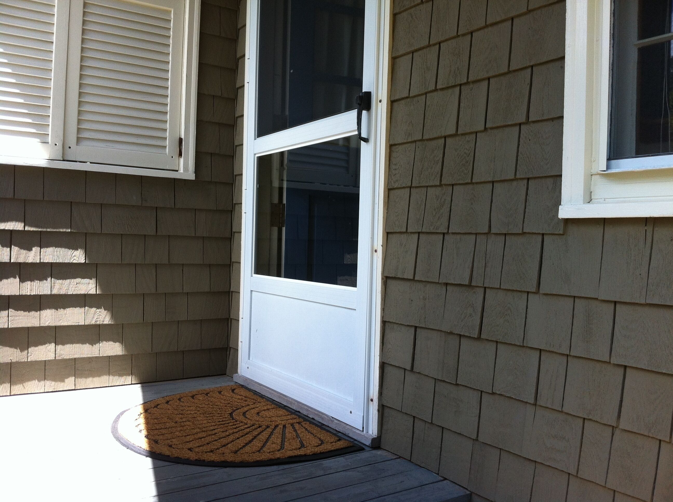 A house corner with a white door, beige siding, and a brown doormat.
