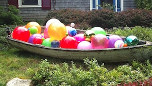 Un bateau rempli de ballons colorés, dans un jardin, avec une maison en arrière-plan.