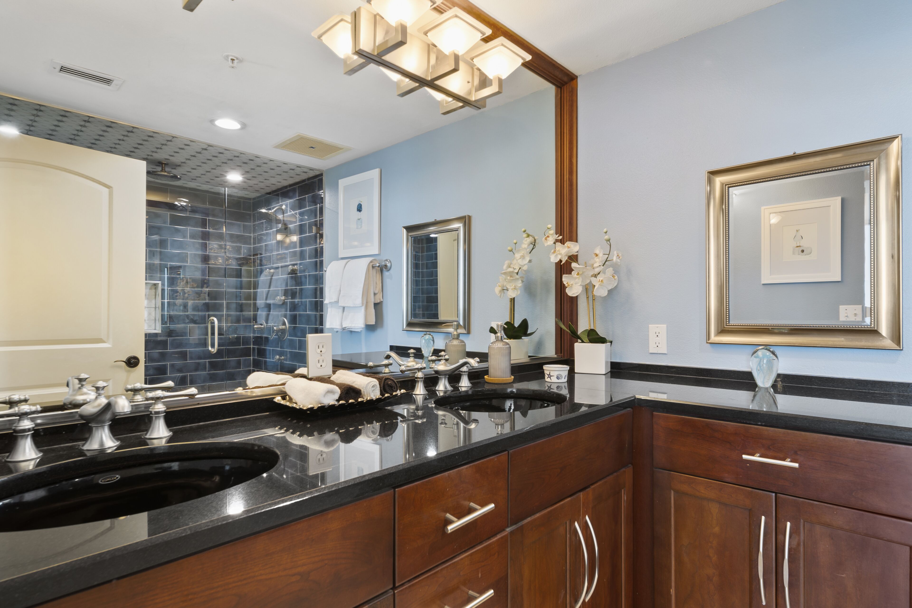 A bathroom with a double sink, wooden cabinets, a large mirror, and blue-tiled walls.
