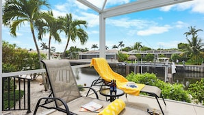 A balcony with a chair, a table, and a yellow towel. There are bottles on the table and a magazine on the chair. - Idyllic Waterfront Home | Pool & Western Exposure (Marco Island)
