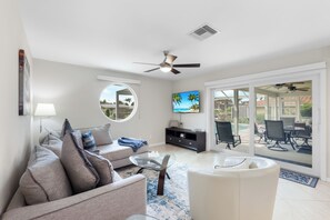 Un salon moderne avec un canapé, une table basse et un téléviseur. Il y a un balcon équipé de mobilier d’extérieur.