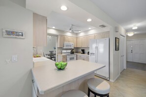 A modern kitchen with white cabinets, a central island, and a ceiling fan.