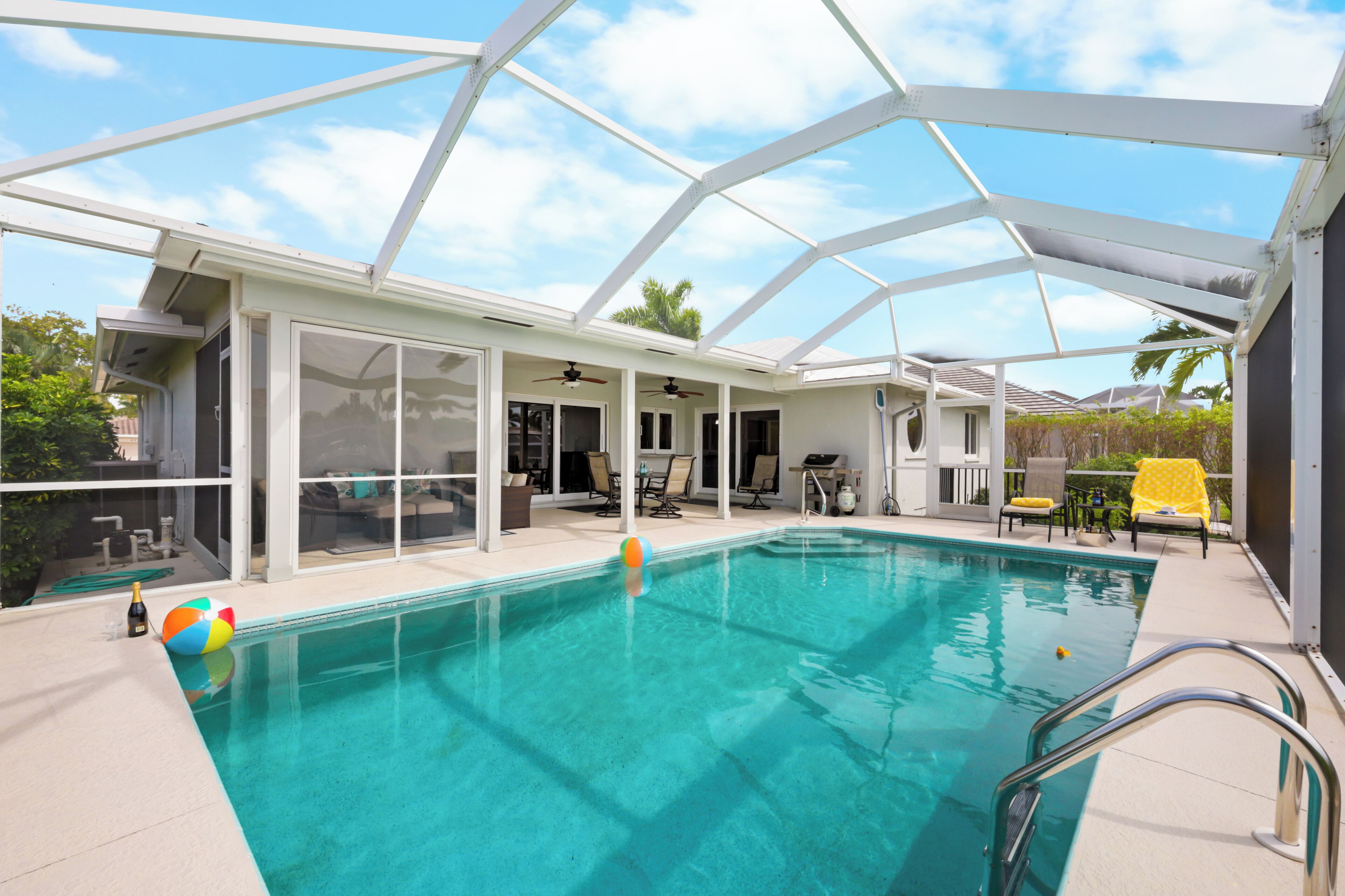 Una piscina interior con agua cristalina azul, techo de cristal y zona de terraza con sillas y mesa.