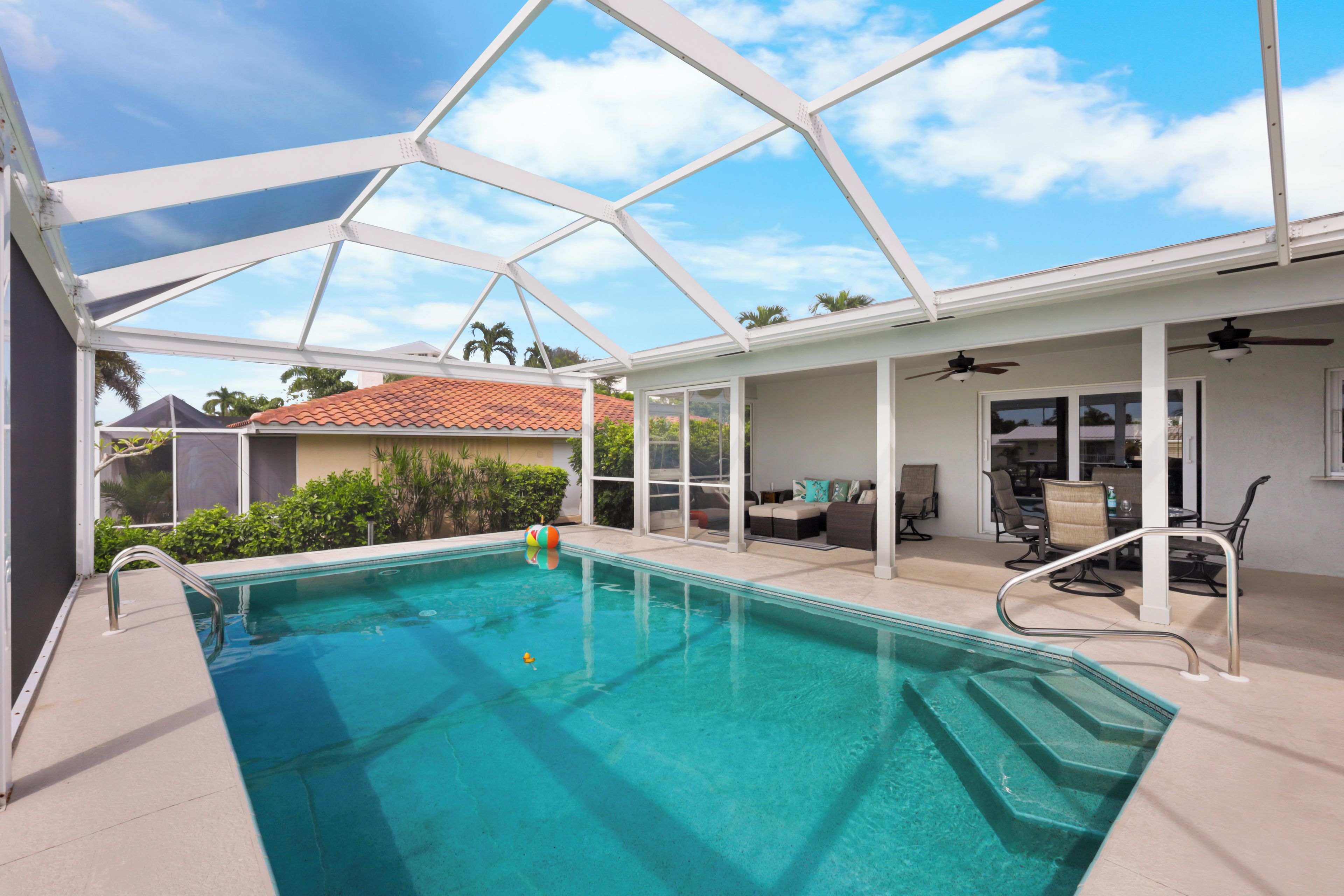 A covered outdoor swimming pool with a glass ceiling, surrounded by a patio area with seating and a kitchen.