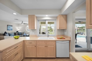 Cocina moderna con armarios de madera, lavavajillas blanco y un ventanal grande.