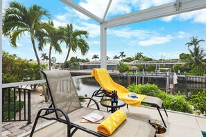 A balcony with a chair, a table, and a yellow towel. There are bottles on the table and a magazine on the chair.