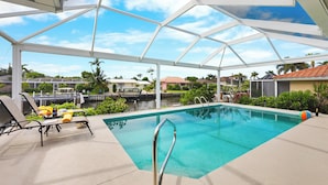 A covered outdoor swimming pool with lounge chairs and a view of the surrounding neighborhood. - Idyllic Waterfront Home | Pool & Western Exposure (Marco Island)