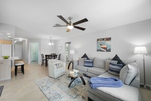 A modern living room with a grey sofa, a glass coffee table, and a ceiling fan. - Idyllic Waterfront Home | Pool & Western Exposure (Marco Island)