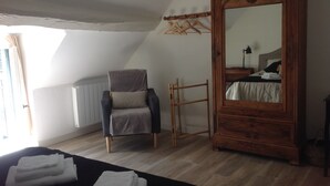 A bedroom with a large wooden wardrobe, a chair with a patterned cushion, a wooden ladder, and a neatly folded bed. - Warm family home (Ménétréol-sous-Sancerre)