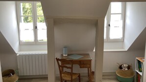 A room with a sloped ceiling, a table with a chair, a radiator, and a window with a view of greenery. - Warm family home (Ménétréol-sous-Sancerre)