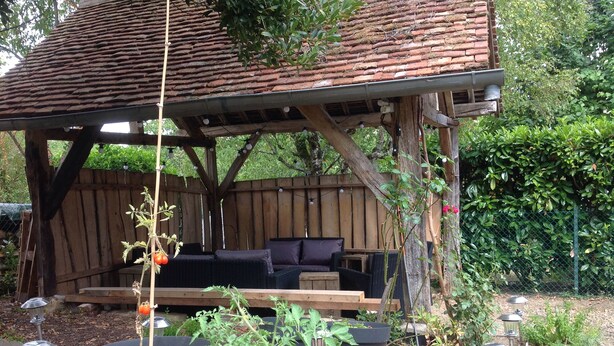 A wooden outdoor seating area with a brick roof, surrounded by potted plants and garden lights. - Warm family home (Ménétréol-sous-Sancerre)