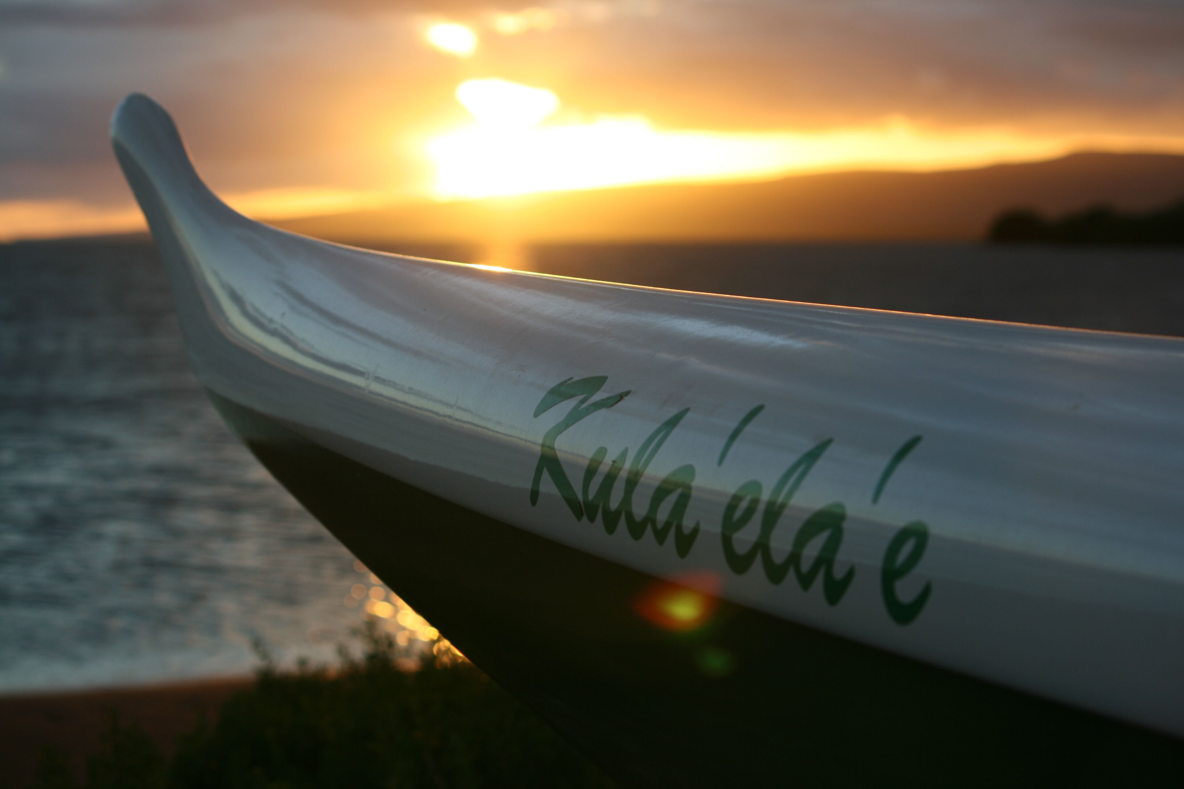 Un bateau portant le nom « Kula'ela'e » sur sa coque, se détachant sur le fond d'un coucher de soleil.