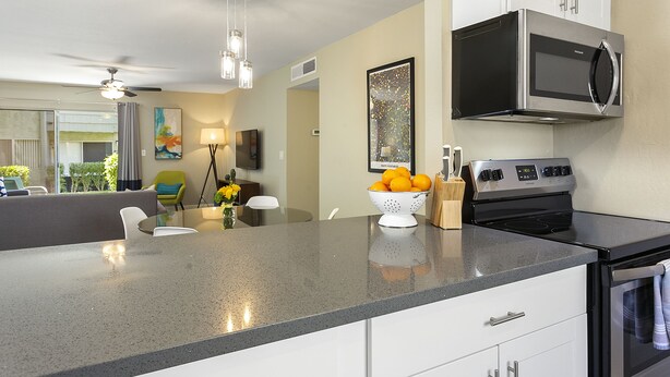 A modern kitchen with a built-in oven, microwave, and a large island with a colander of oranges.