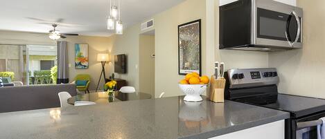 A modern kitchen with a built-in oven, microwave, and a large island with a colander of oranges.