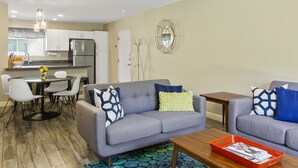 A modern living room with a grey sofa, a coffee table, and a dining area with a round table and chairs.