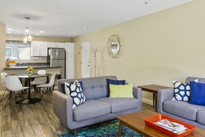Uma sala de estar moderna com um sofá cinzento, uma mesa de centro e uma área de jantar com uma mesa redonda e cadeiras.