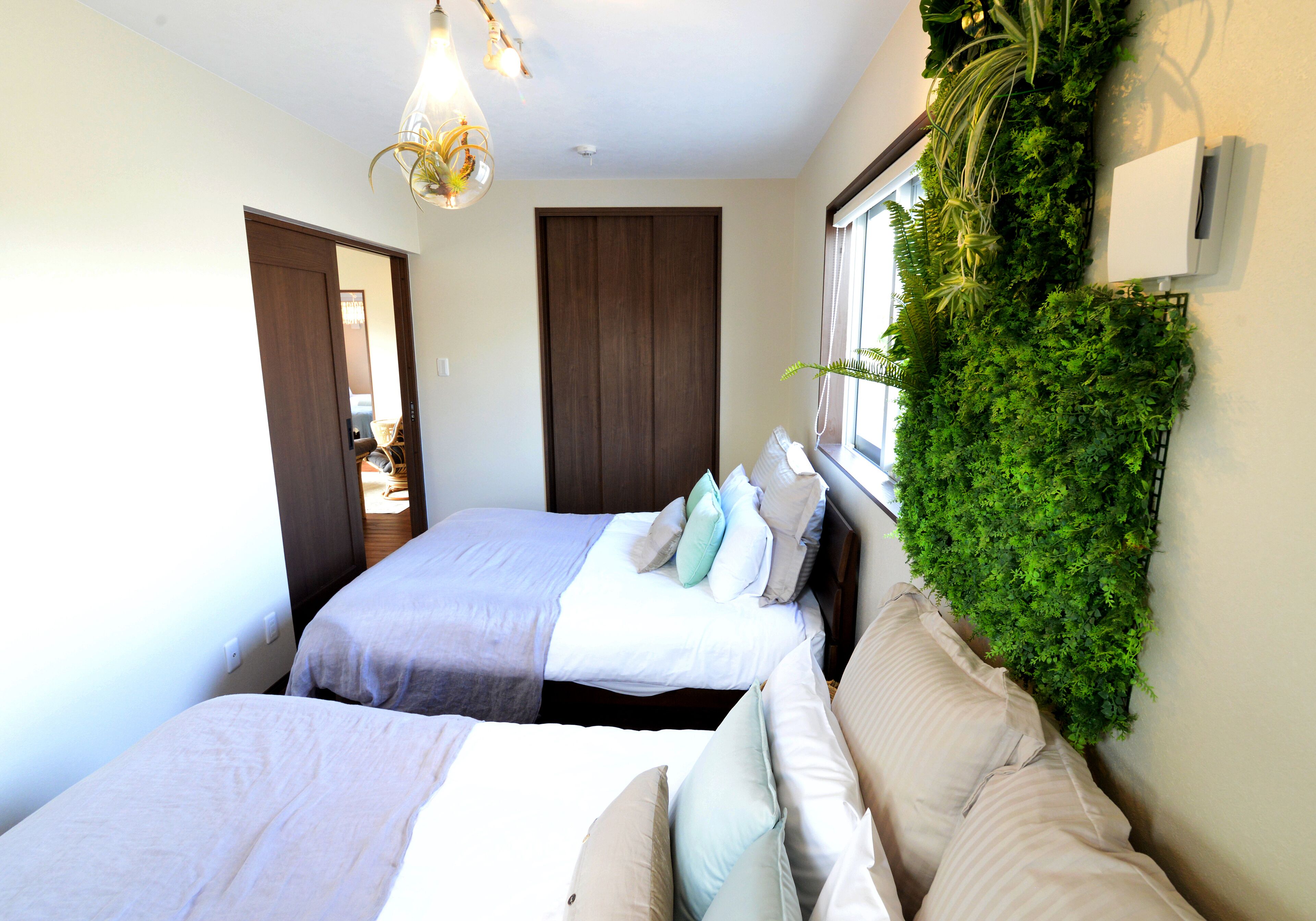 A bedroom with two beds, a window with a view, a wall-mounted plant, and a ceiling light fixture.