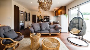 A modern living room with a sofa, two wicker chairs, a hanging chair, and a unique woven light fixture. - BB Wakugawa Terrace (Nakijin)