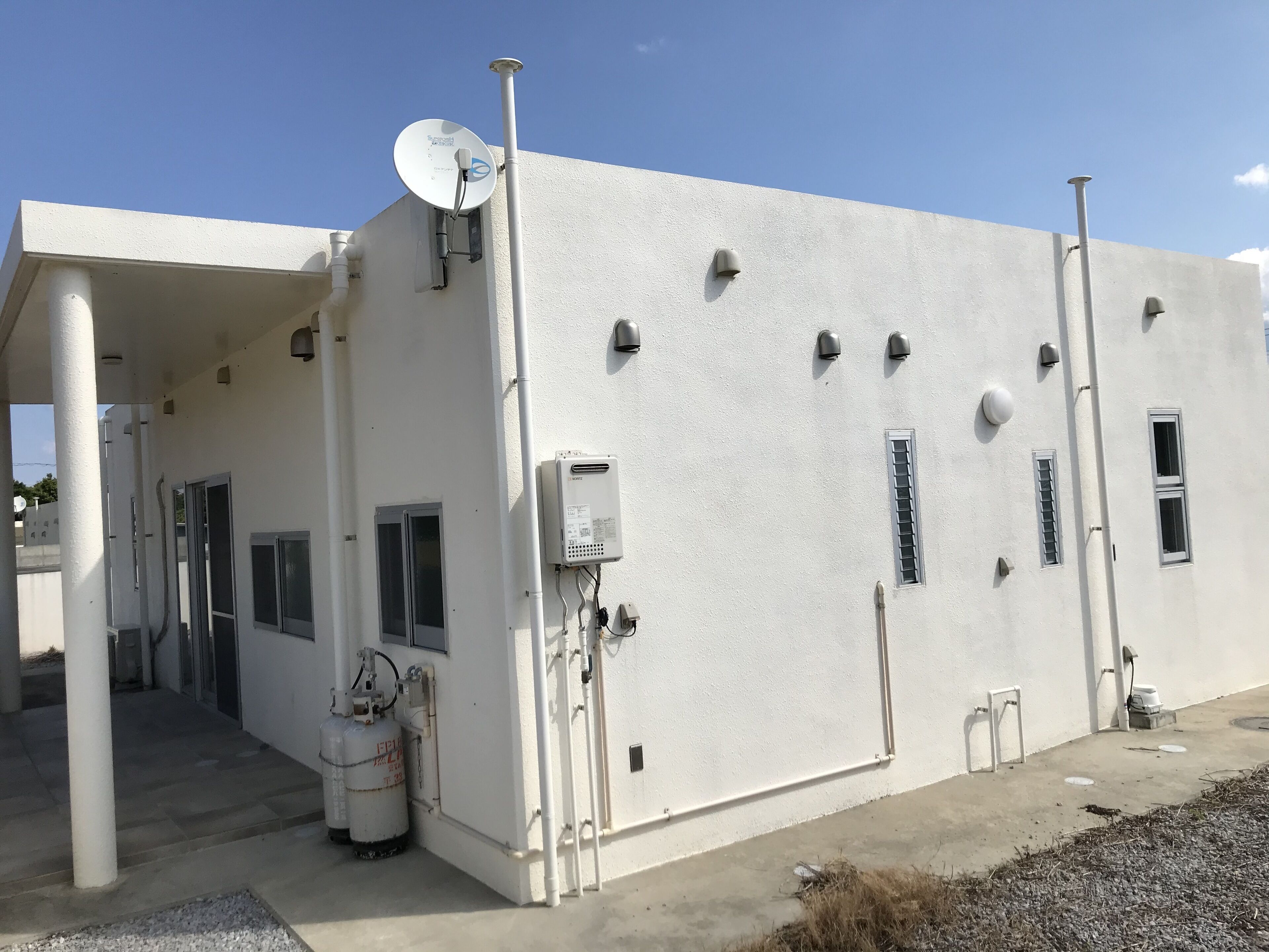 A white industrial building with a satellite dish, multiple windows, and a large white tank.
