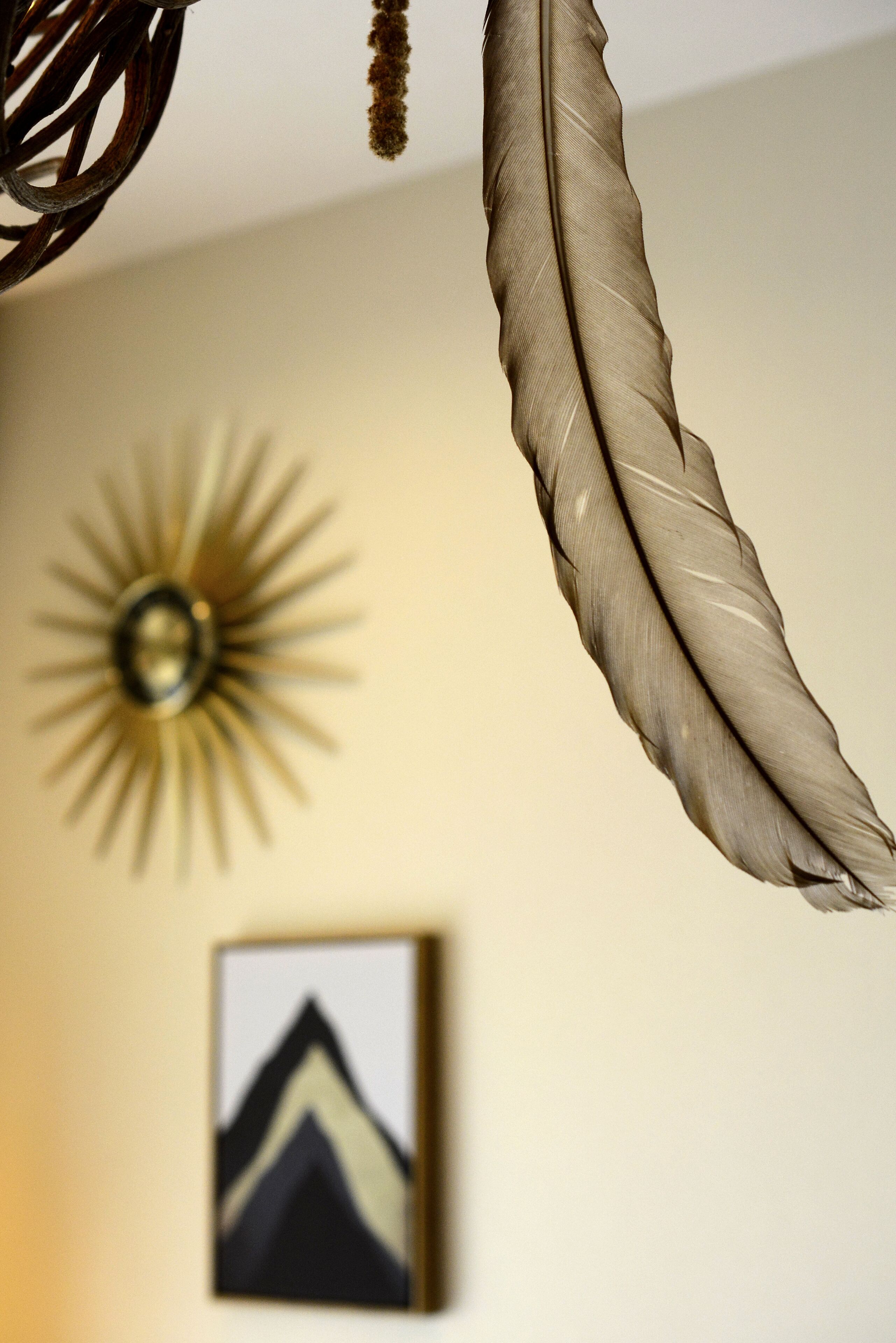 Una pluma colgando de un accesorio del techo, una decoración mural con diseño de sol y un cuadro en la pared.