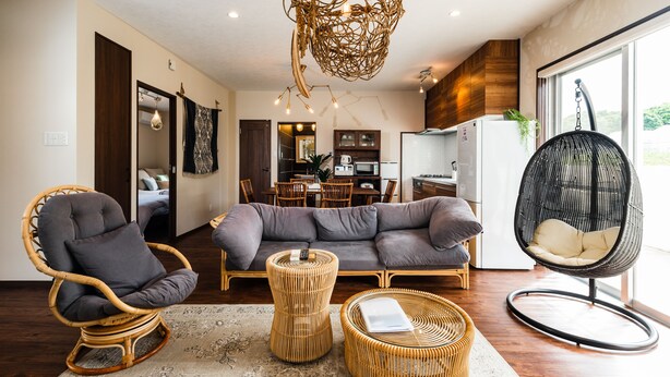 A modern living room with a grey sofa, wicker chairs, and a hanging chair. - BB Wakugawa Terrace (Nakijin)