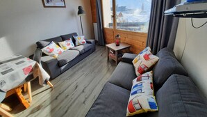 En hyggelig stue med en grå sofa, et lille bord og et vindue med udsigt til bjerge.